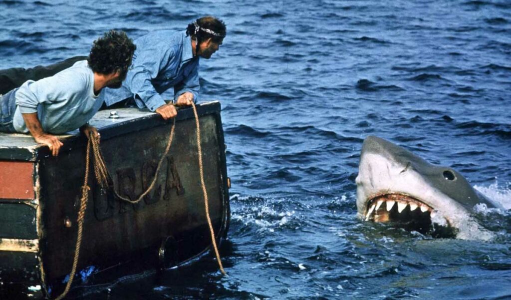 Scène de JAWS (1975) où le requin attaque le bateau Orca alors que deux hommes observent depuis la poupe. 